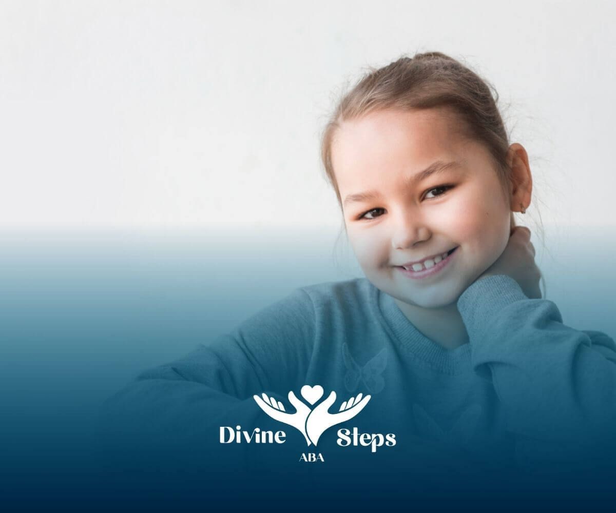 Smiling girl with autism sitting at a table with her hand on her neck.