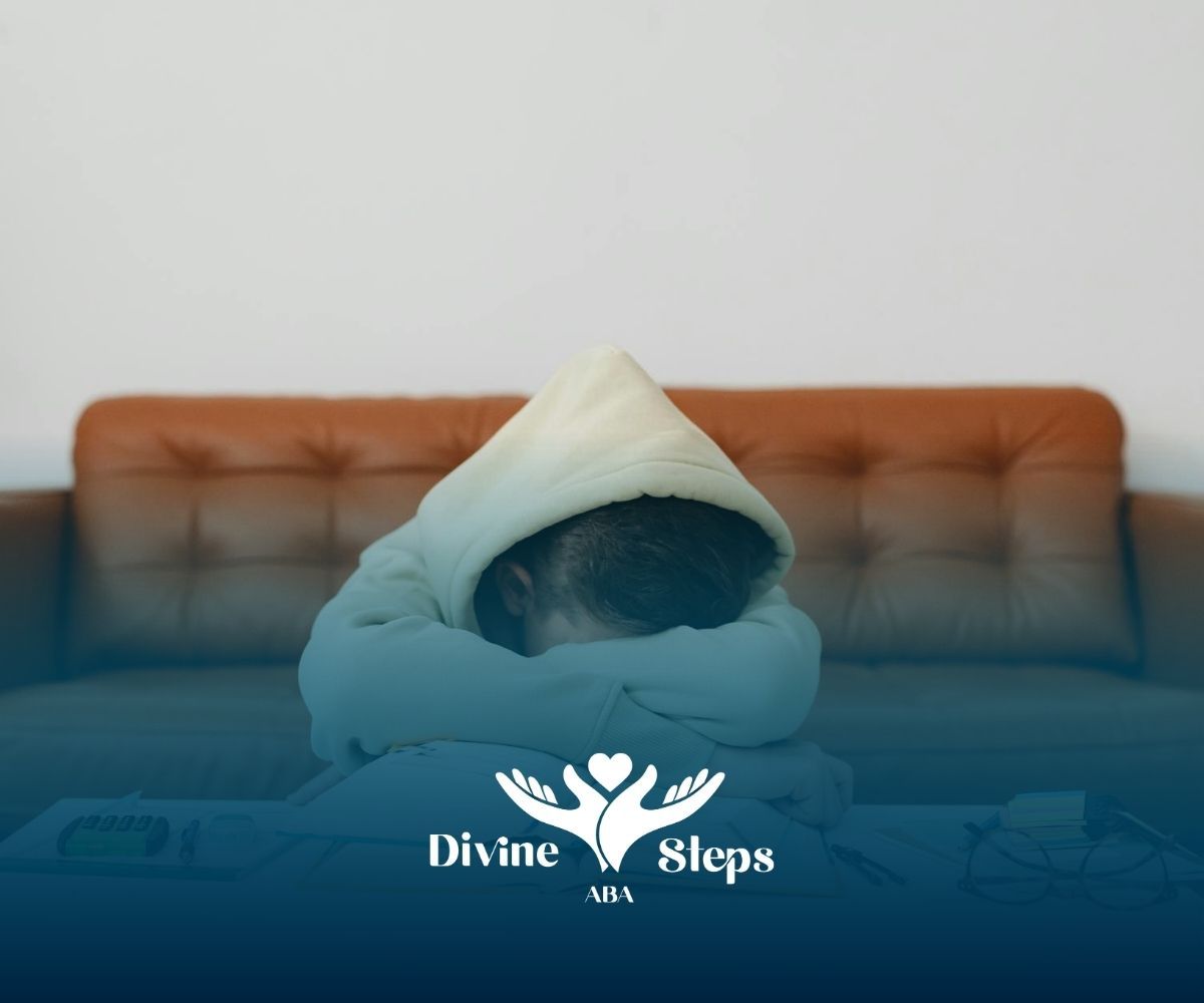 An autistic student in hoodie resting on open book during ABA therapy session in North Carolina.