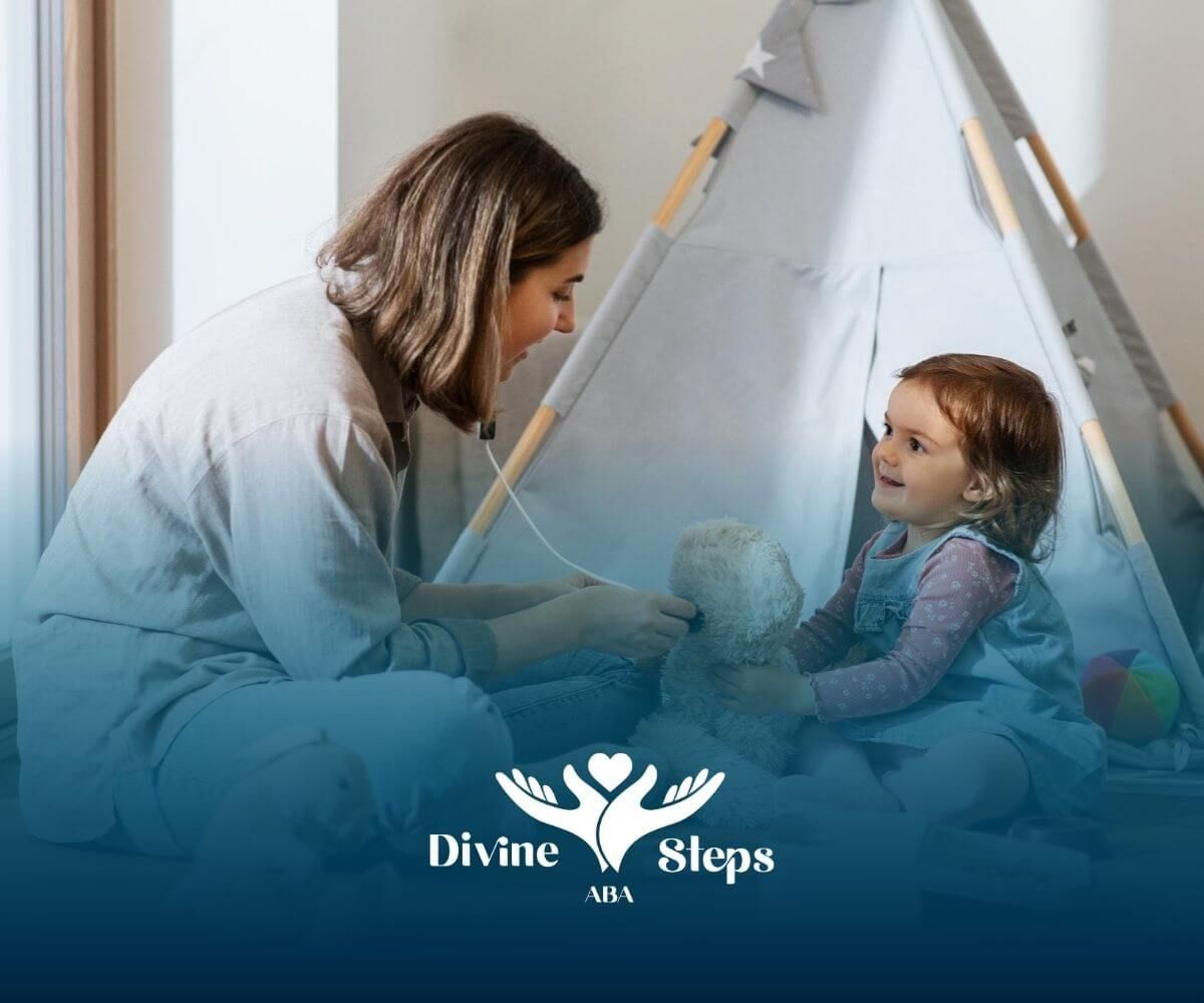 An ABA therapist and a little girl are sitting on the floor playing with a teddy bear in ABA therapy