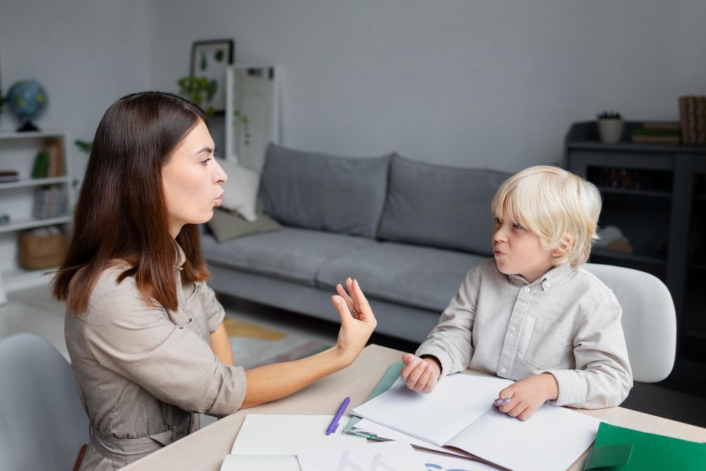 Woman and boy at a table, woman gestures, boy looks on. Living room setting.