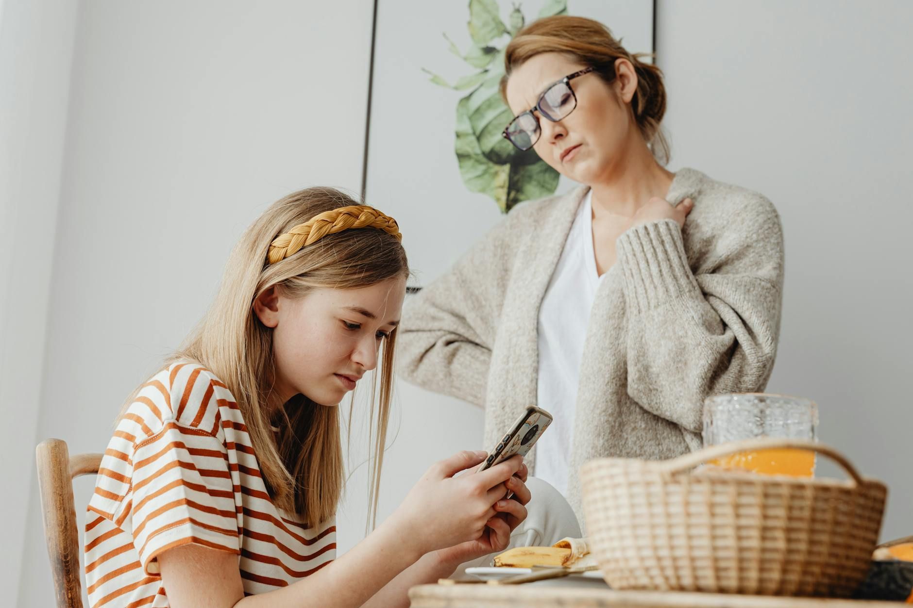 Concerned mother watching her autistic daughter focused on a phone at the breakfast table in VA.