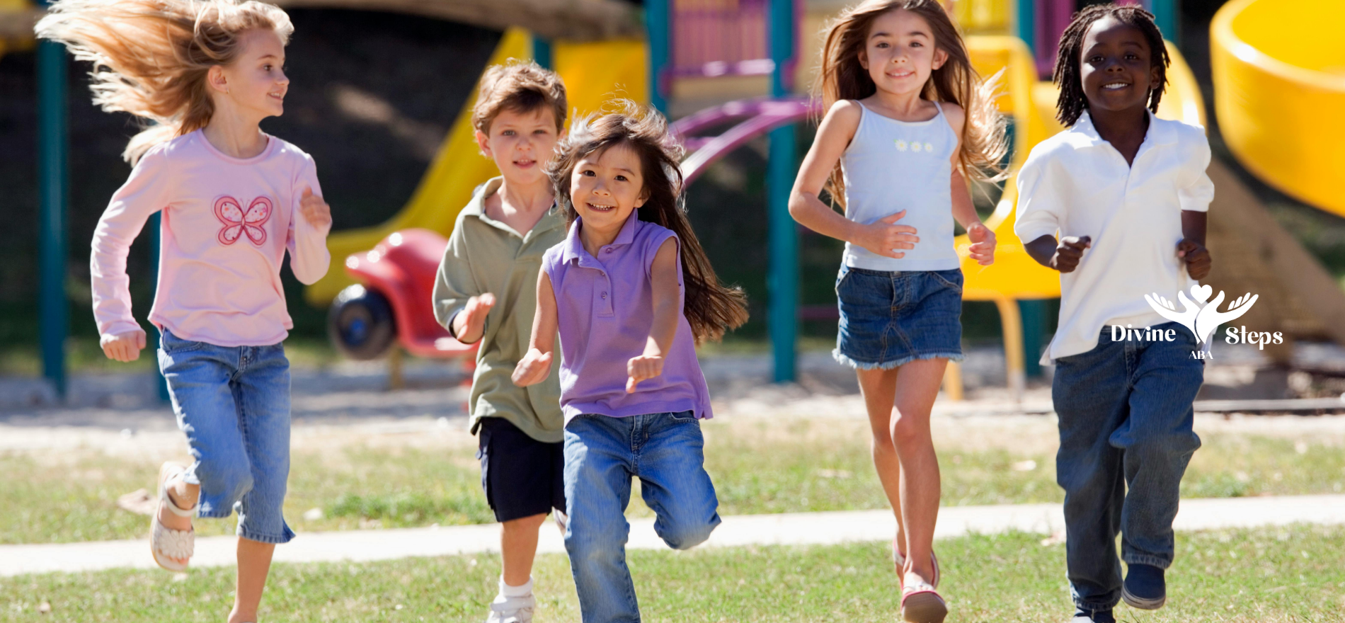 Children running on grass near a playground. They are smiling.