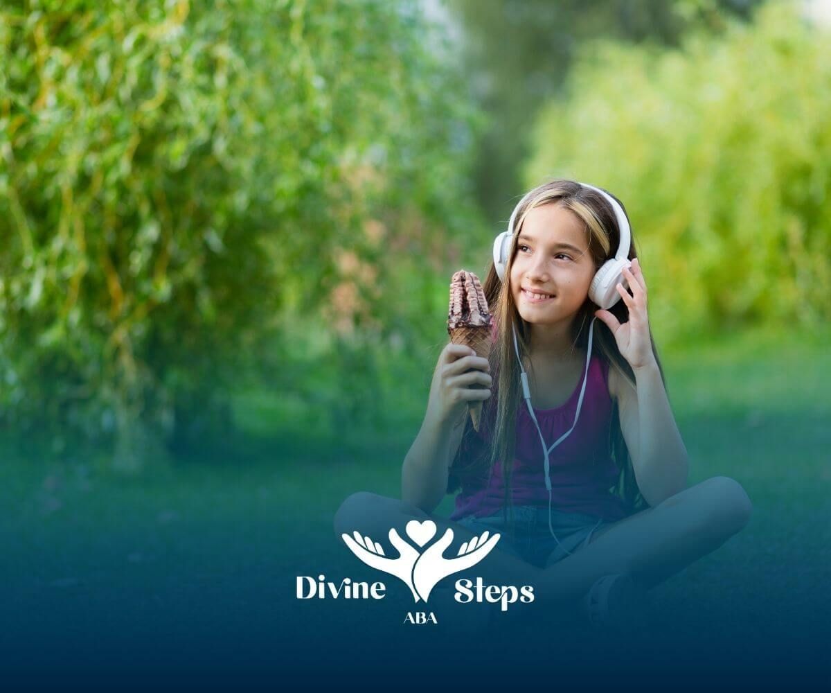 An autistic girl sitting on grass with headphones and ice cream, and enjoying sensory input.