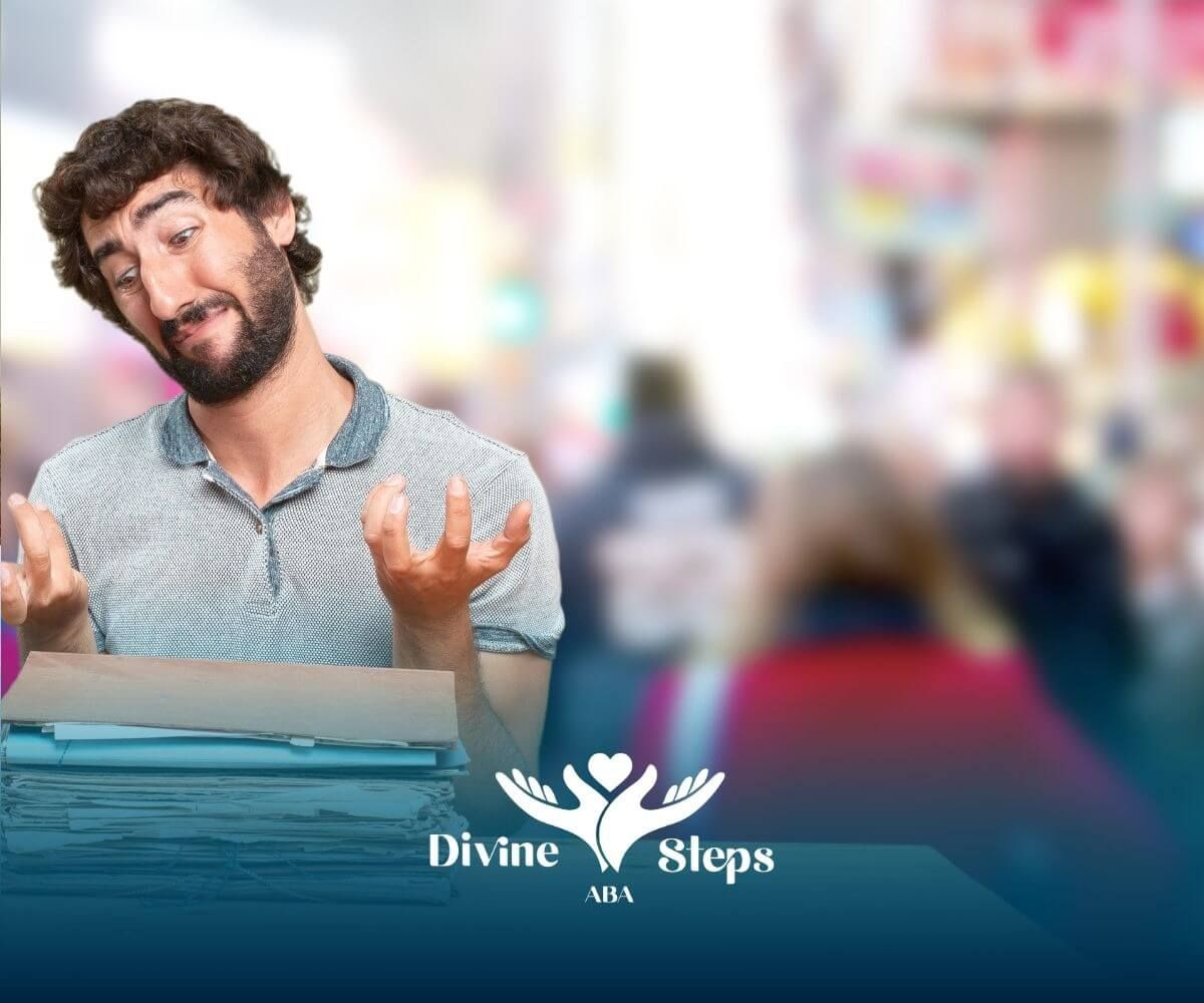 A male therapist with a beard in a casual shirt standing at a desk covered with paperwork.