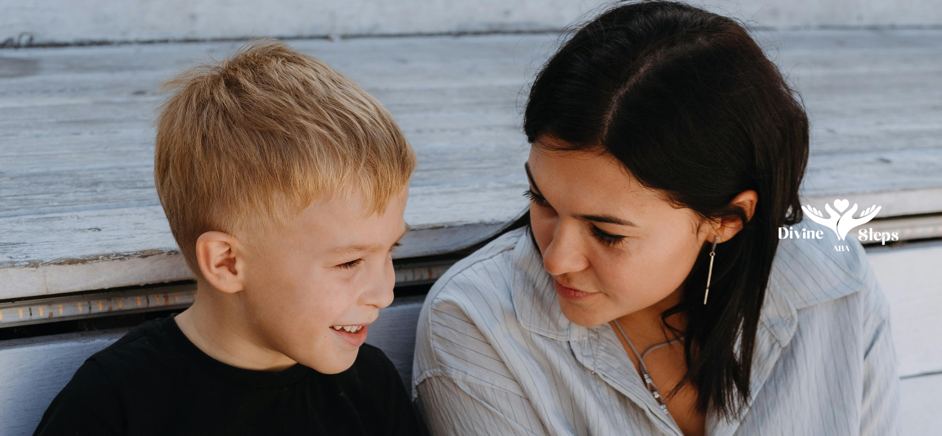 A young person in a black shirt smiles at someone sitting next to them, both look engaged.