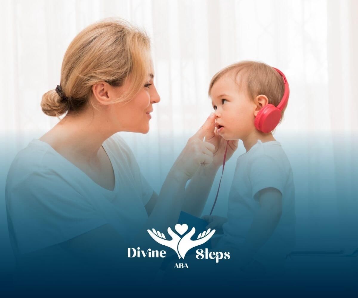 A BCBA playfully interacting with a toddler with autism wearing pink headphones in ABA therapy.