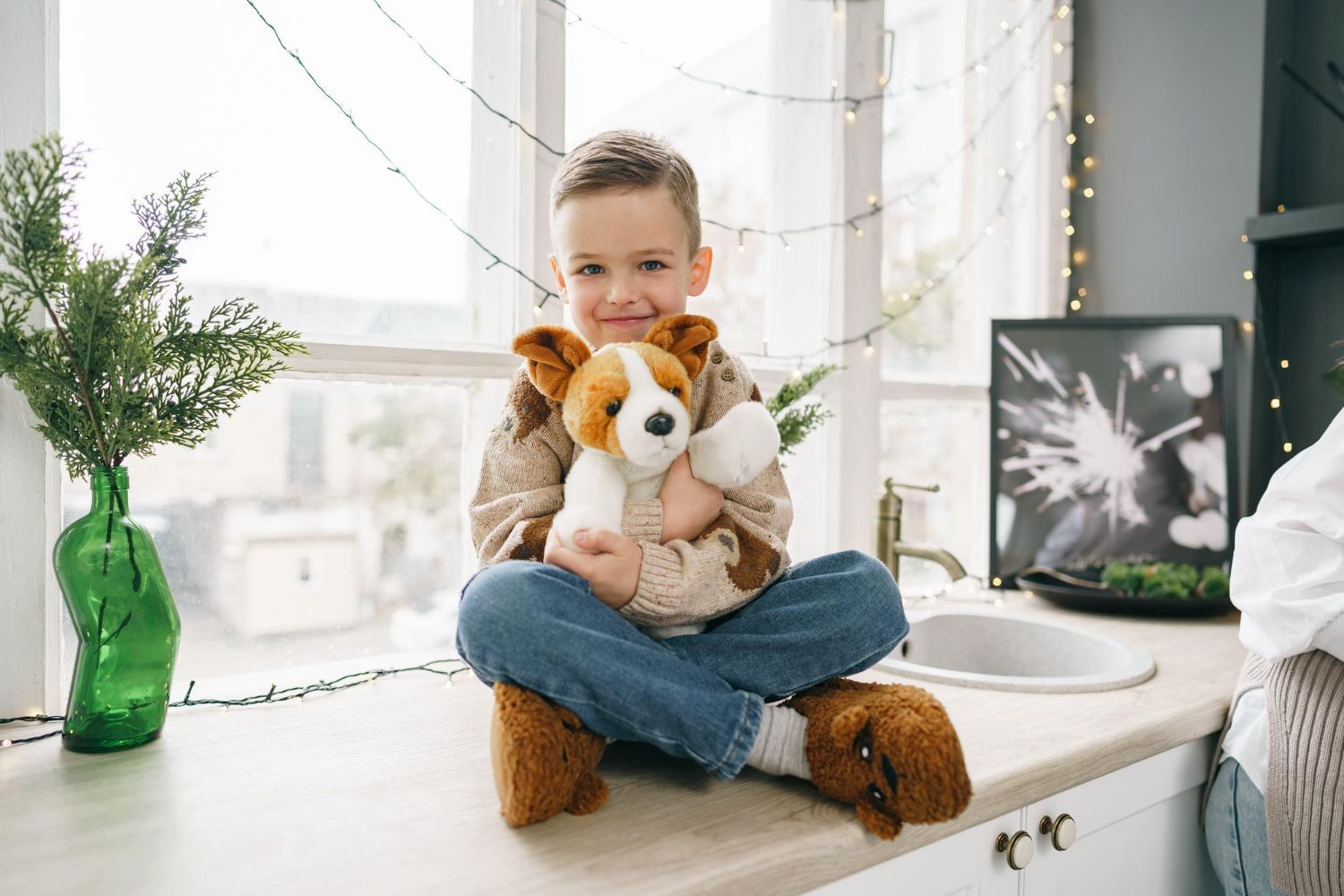 An autistic boy is sitting on a counter holding a stuffed dog.