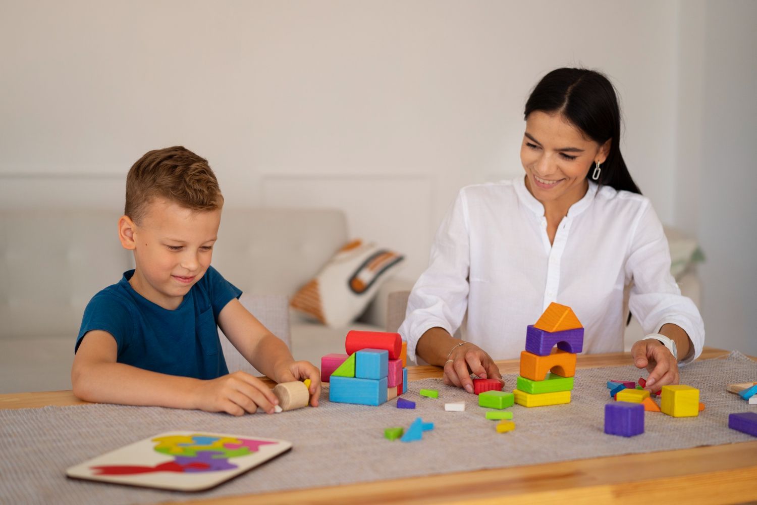 An RBT and a boy are playing with wooden blocks at a table.