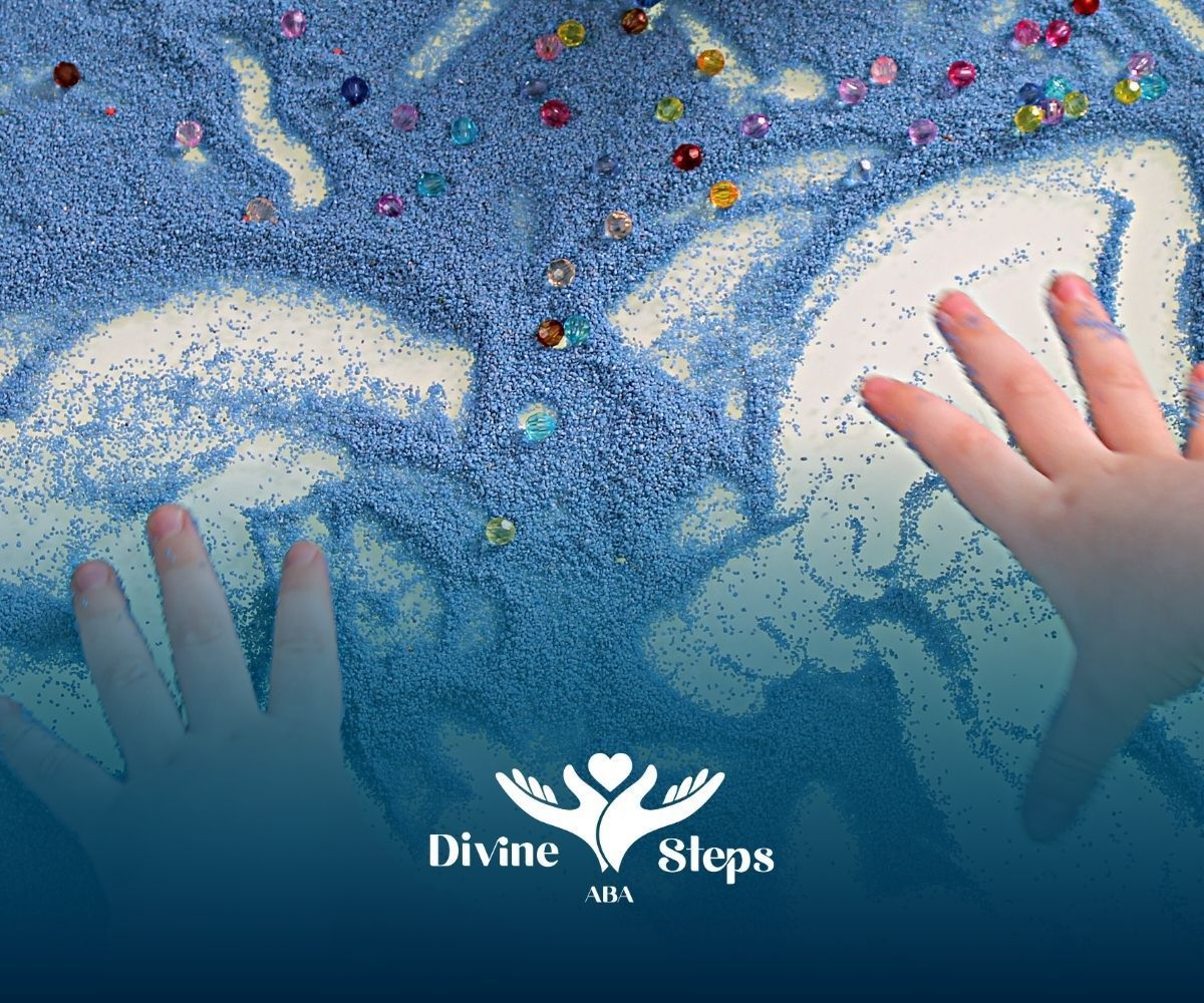 Hands tracing shapes in blue kinetic sand sprinkled with jewels; Divine Steps USA logo at bottom.