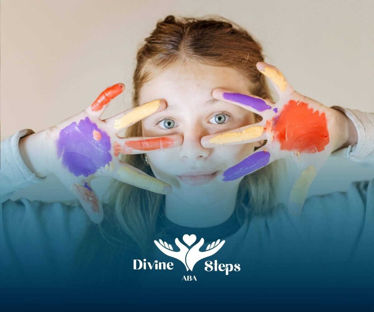 Creative autistic young girl showing hands covered in bright paint after enjoying an art activity.