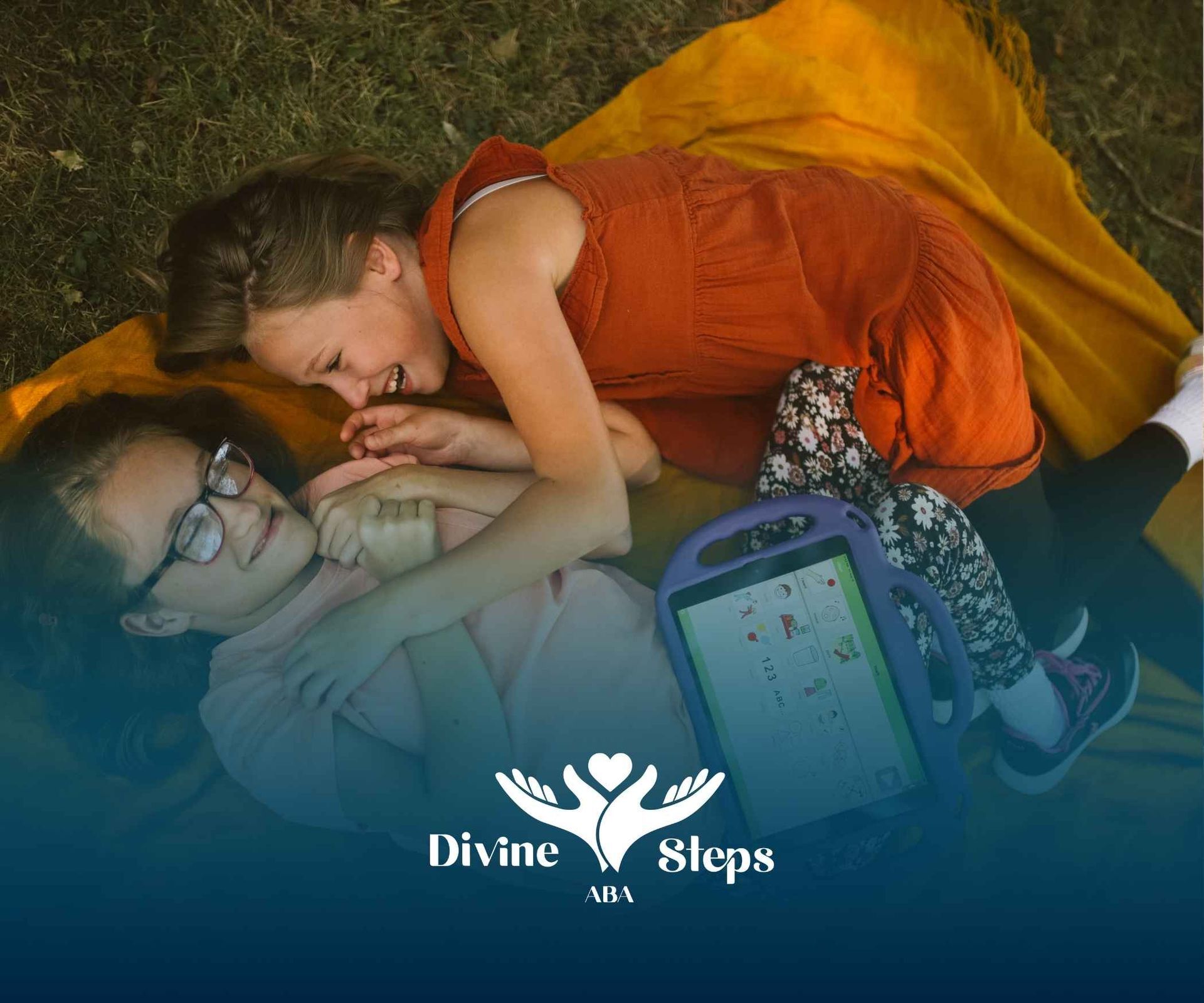 Two young girls are laying on a blanket with a tablet.