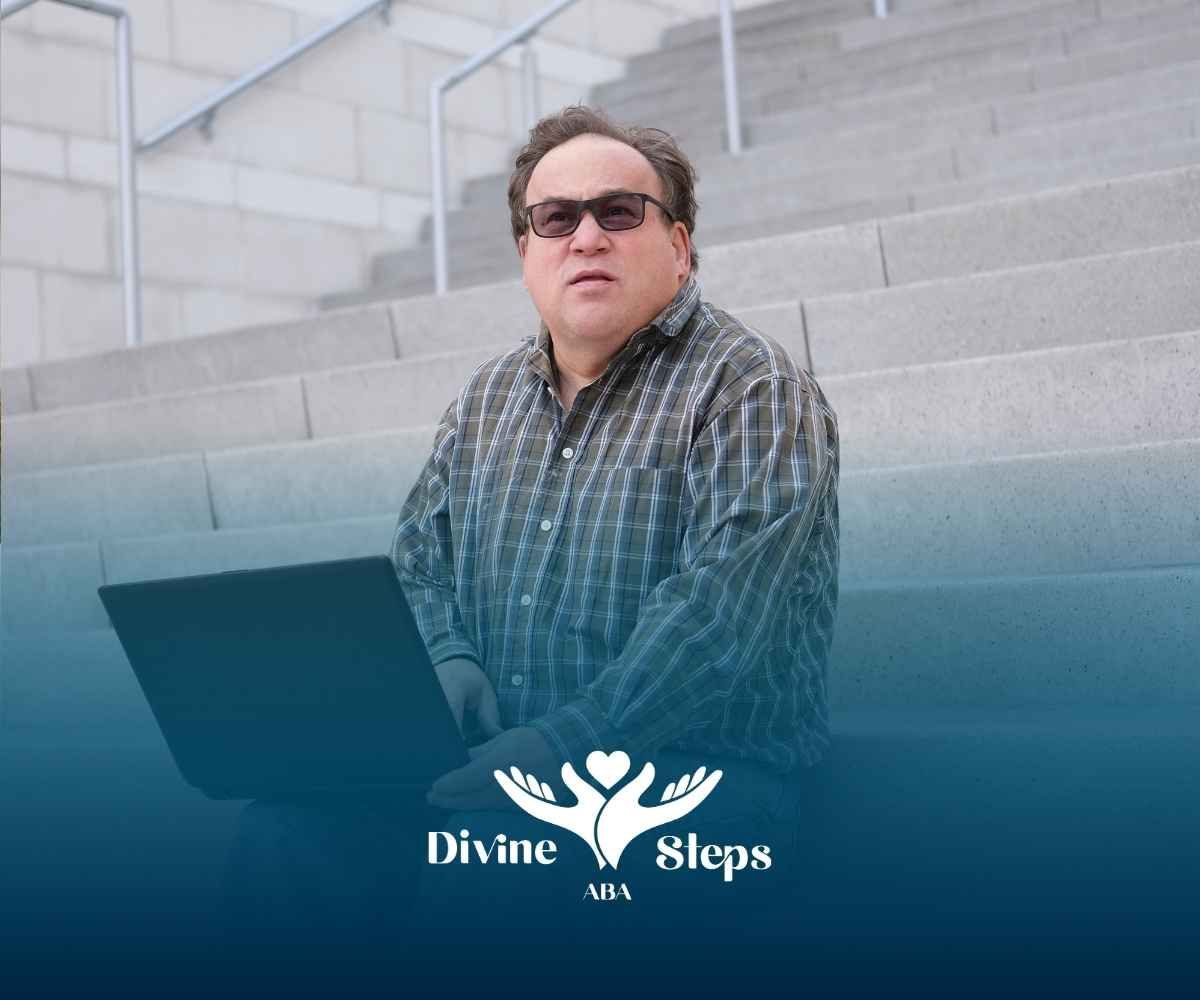 Man with glasses and laptop sits on outdoor steps.