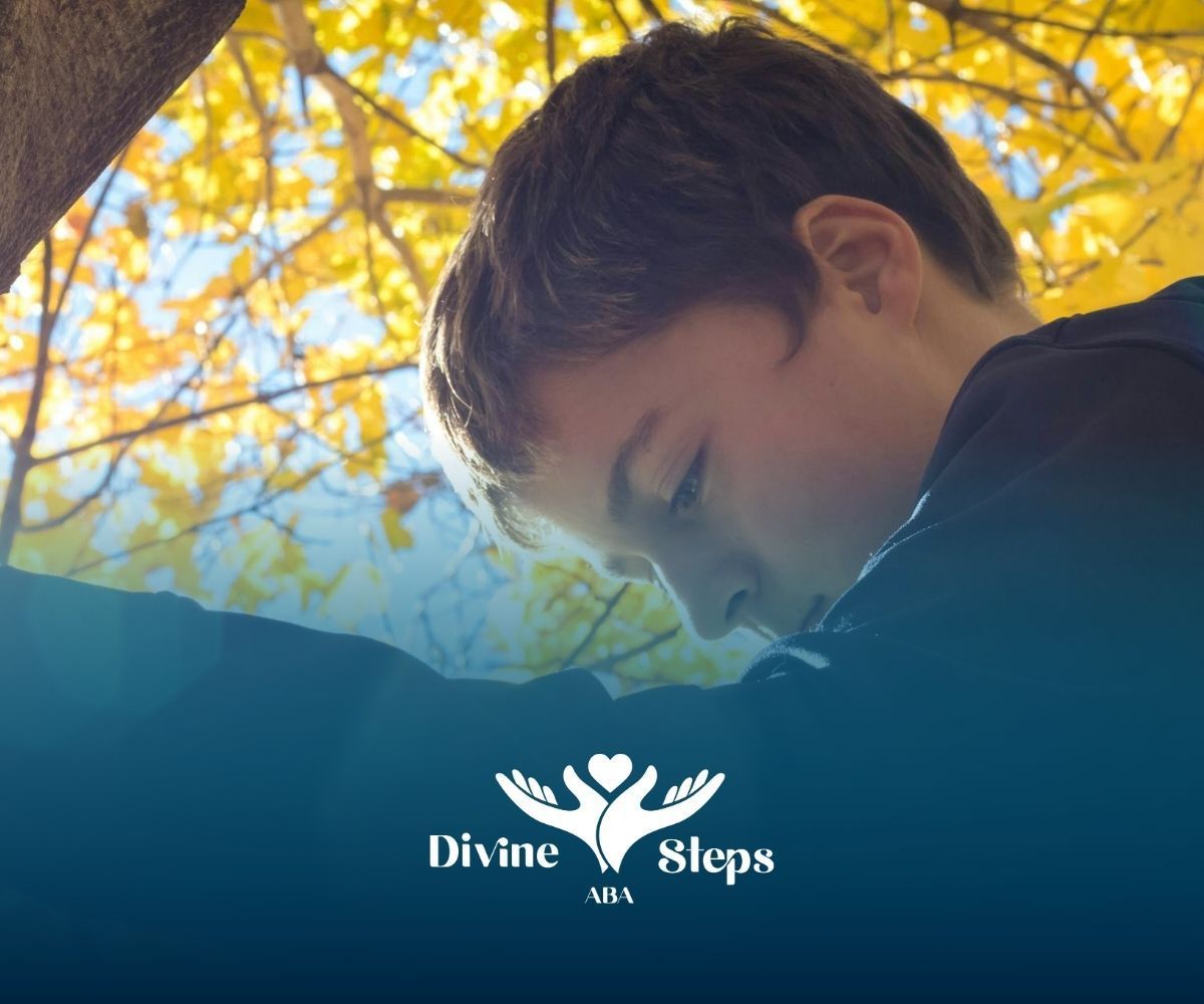 A boy with regressive autism leaning against a tree under bright yellow autumn leaves in NC.