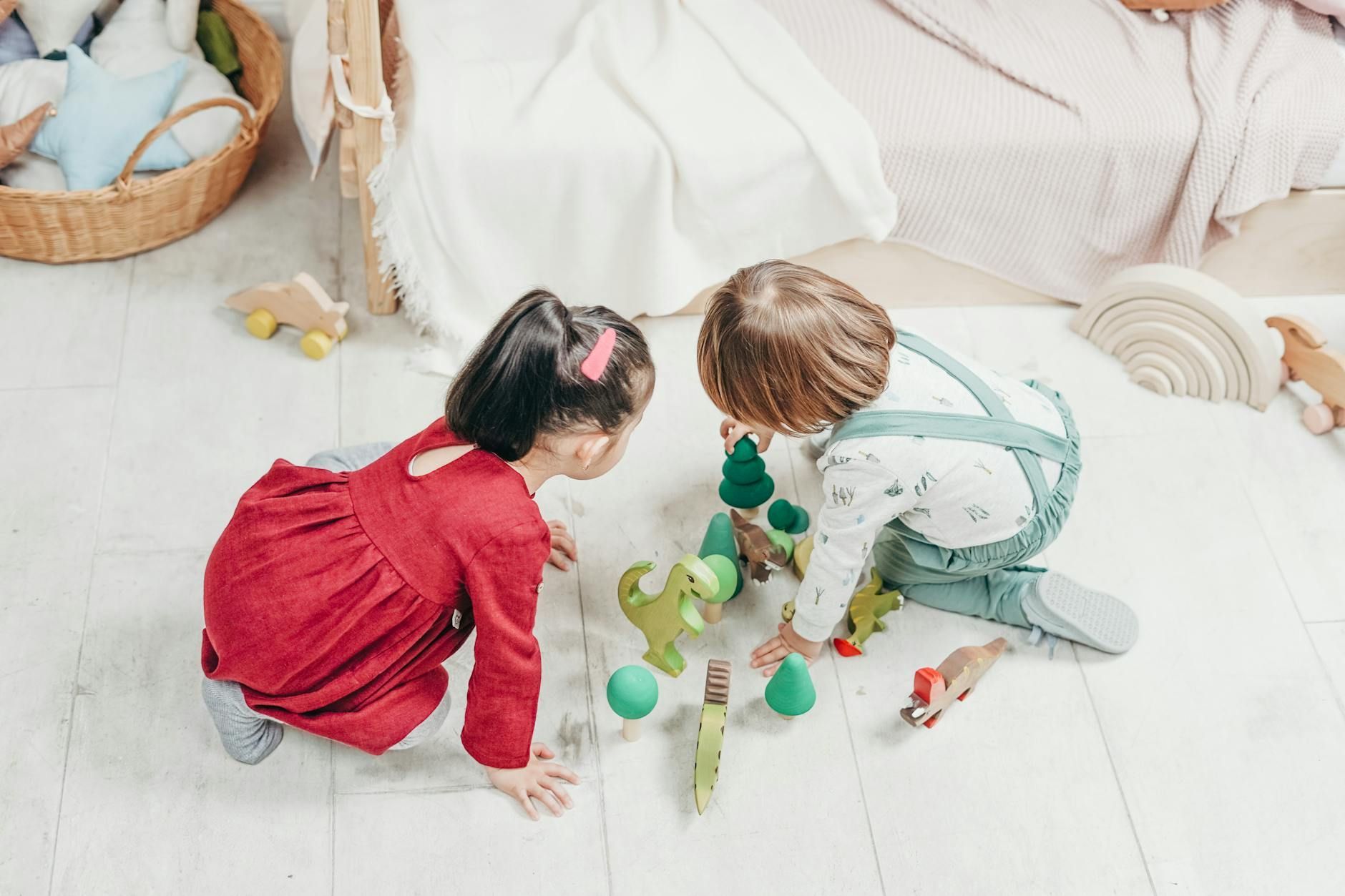 Two autistic children playing with wooden toy dinosaurs and trees on the floor in New Jersey.