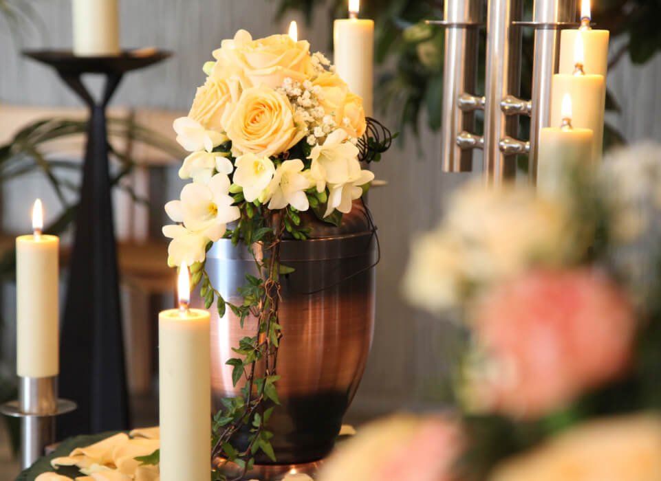 cremation urn made of bronze covered in white rose spray surrounded by candles