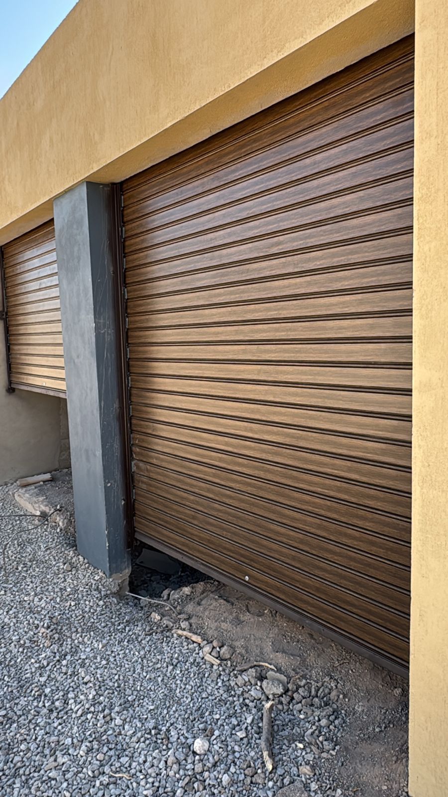 Puertas enrollables de metal marrón se abren parcialmente en un edificio con suelo de grava.