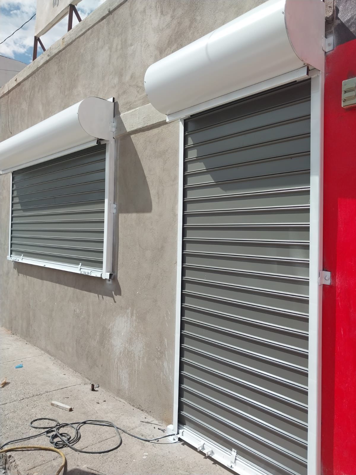 Persianas de seguridad de metal gris en un edificio, que protegen una ventana y una puerta.