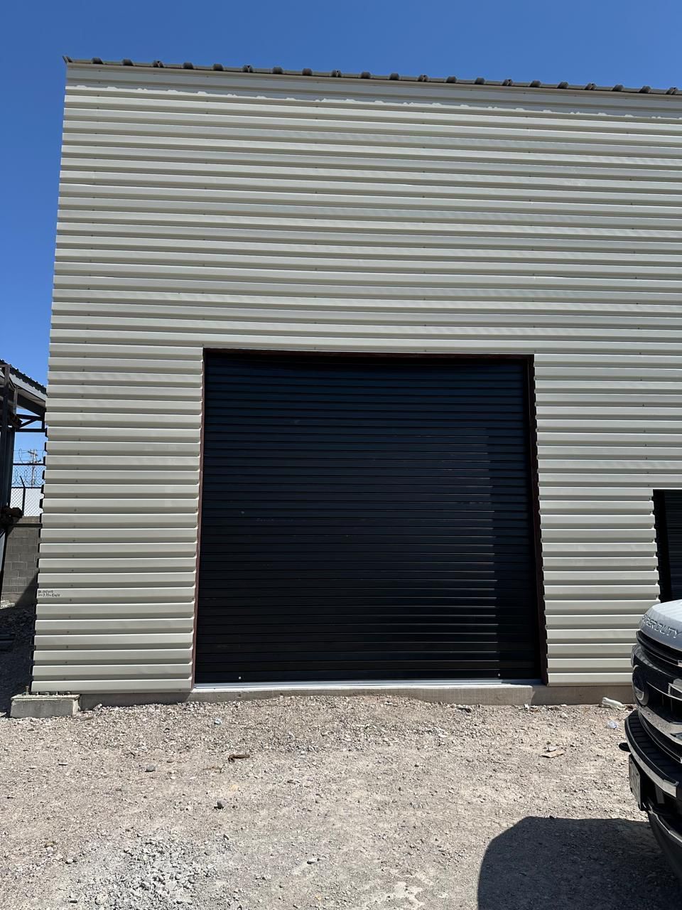 Puerta de garaje negra sobre un edificio de metal corrugado de color marrón bajo un cielo azul claro.