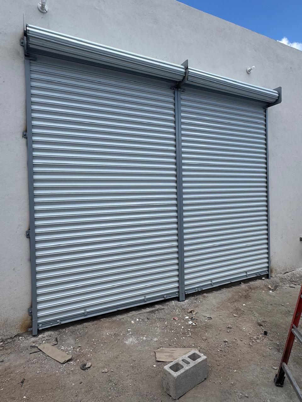 Puertas de seguridad enrollables corrugadas de color gris sobre una pared de hormigón.