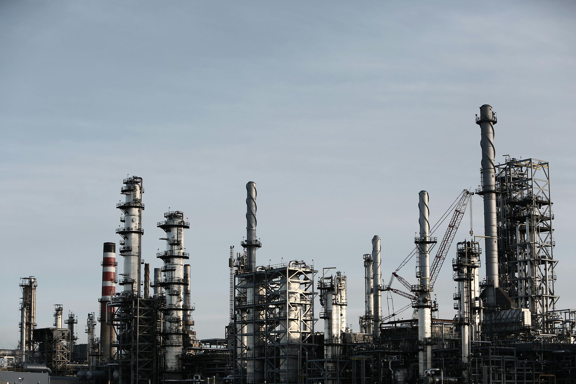 Oil refinery with numerous smokestacks and structures against a pale blue sky.