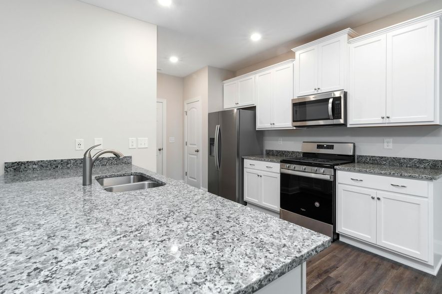 Black metal chairs surround a table in a kitchen with gray cabinets and a wooden countertop.