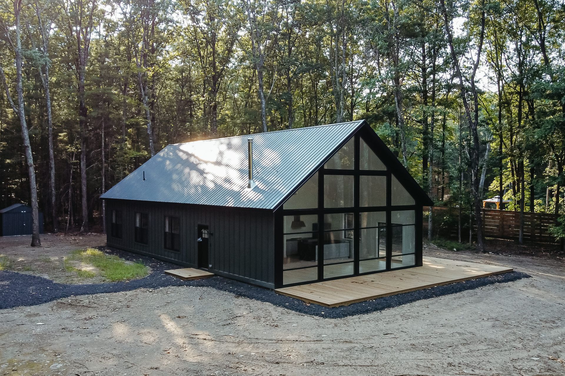 A large black house with a lot of windows is in the middle of a forest.