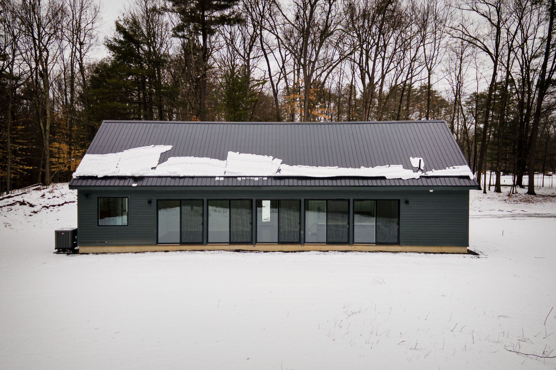 A black house is sitting in the middle of a snow covered field.