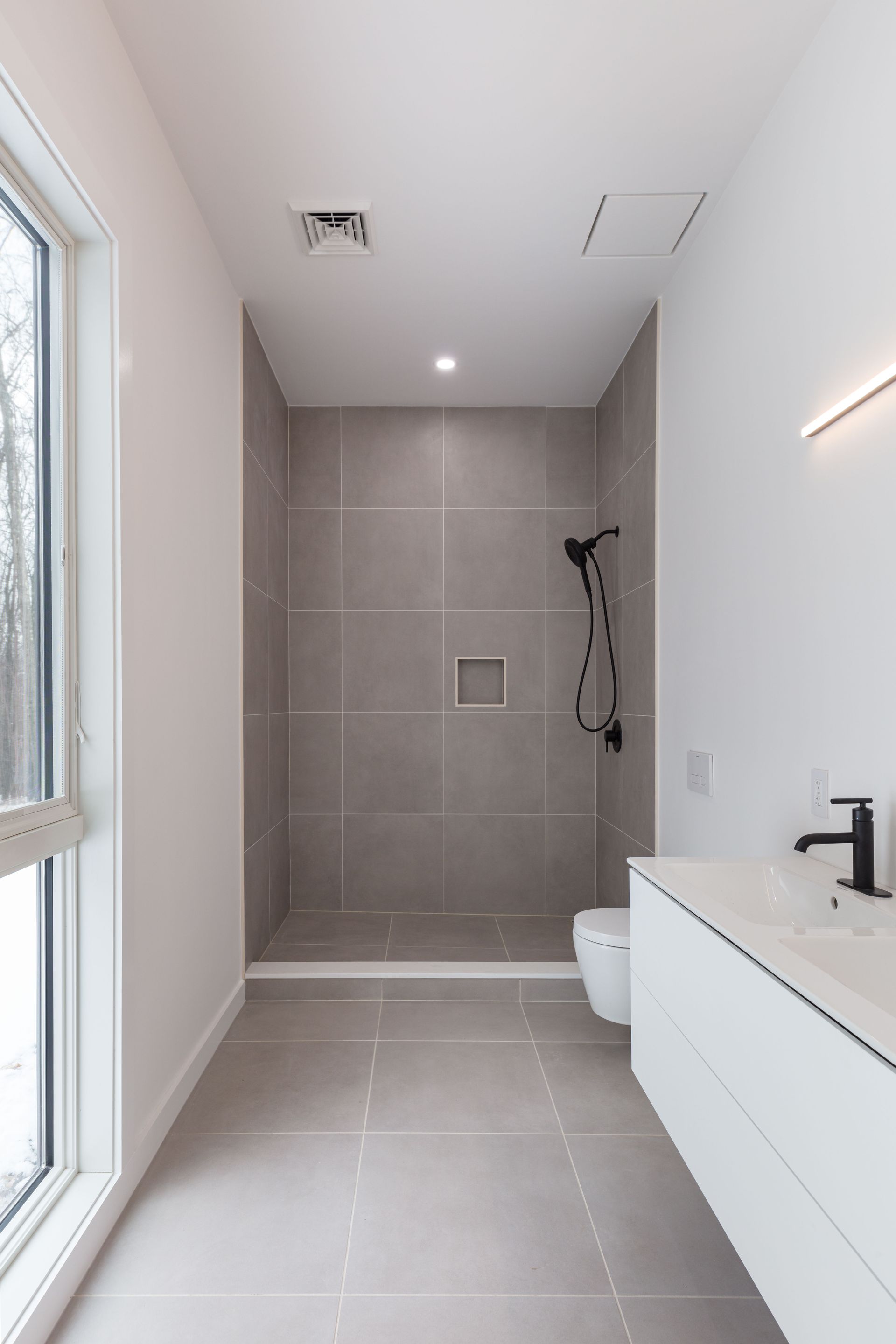 A bathroom with a walk in shower , toilet , sink and window.