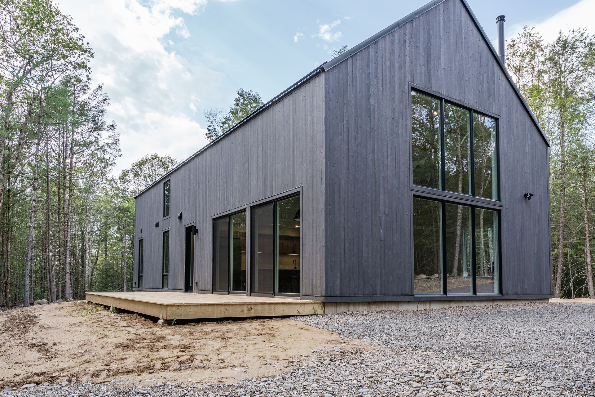 A black house with a lot of windows is sitting in the middle of a forest.