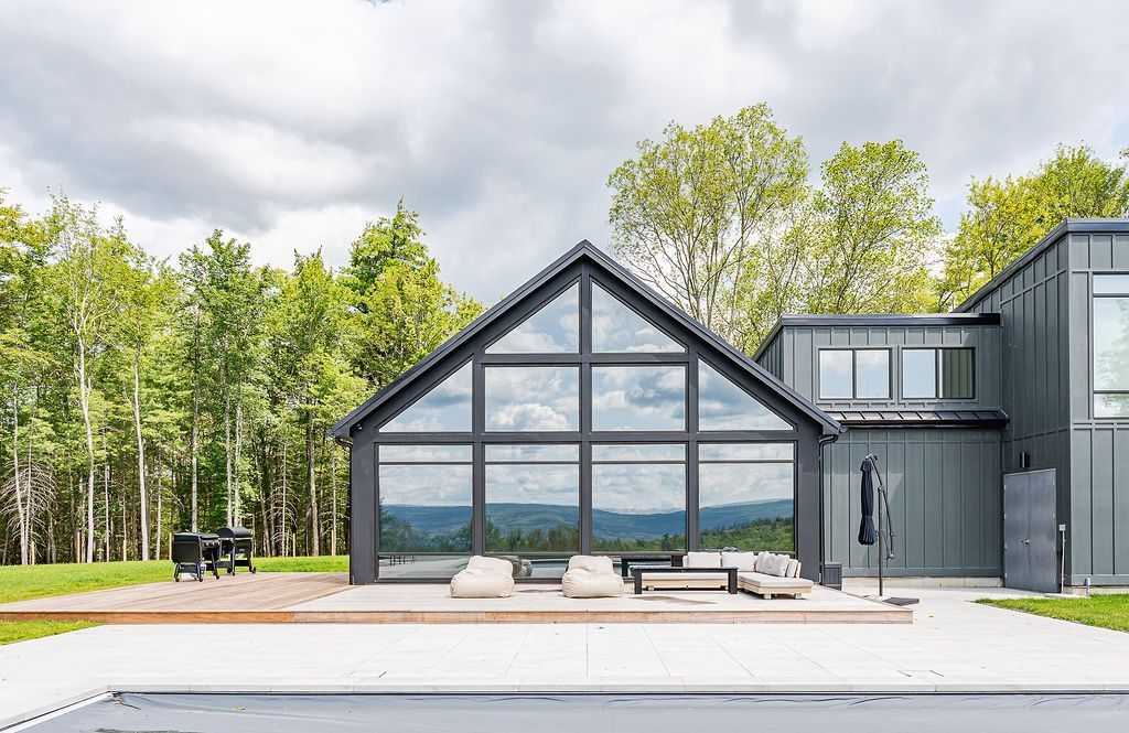 A large gray house with a lot of windows is surrounded by trees.