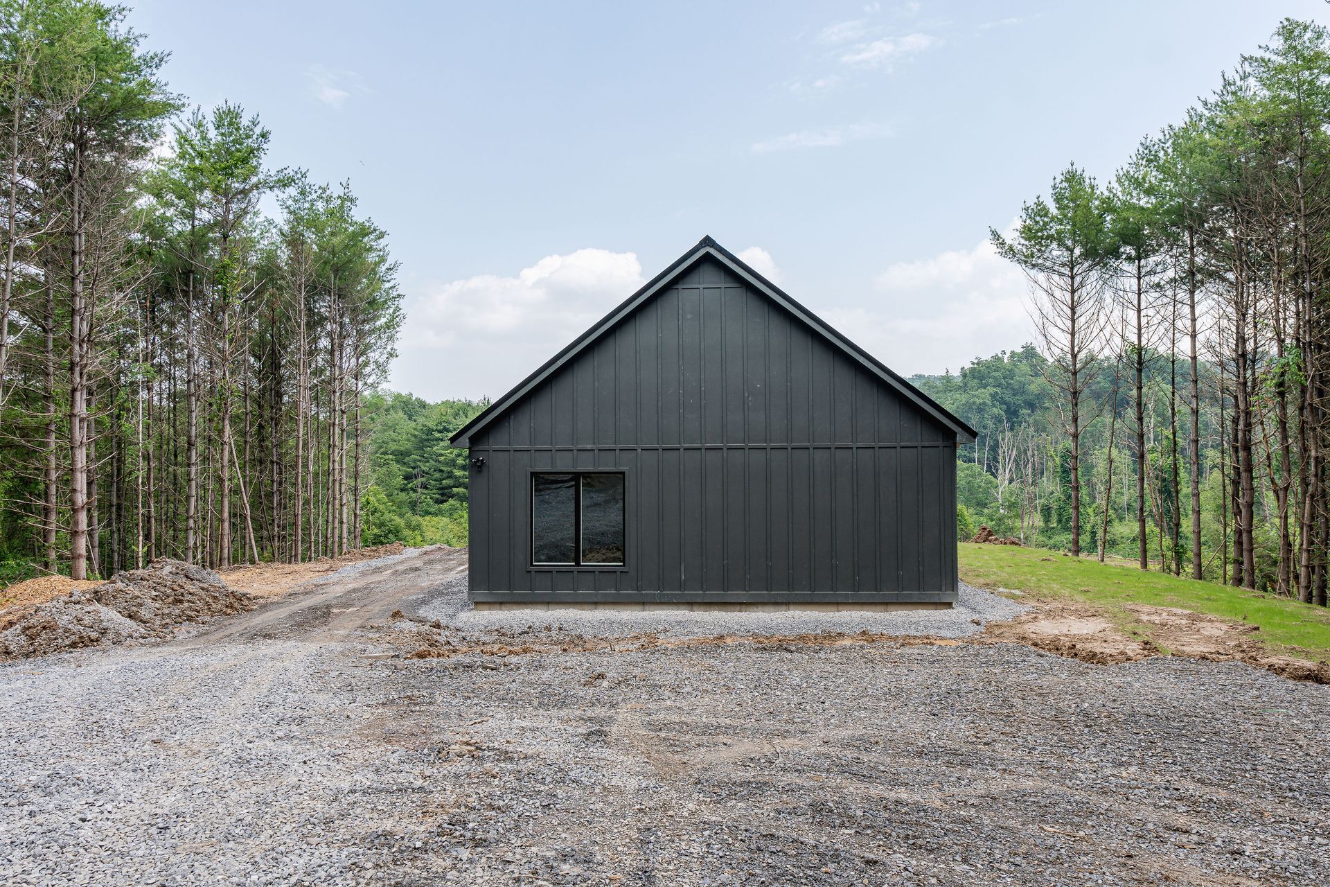 A black house is sitting on top of a gravel road in the middle of a forest.
