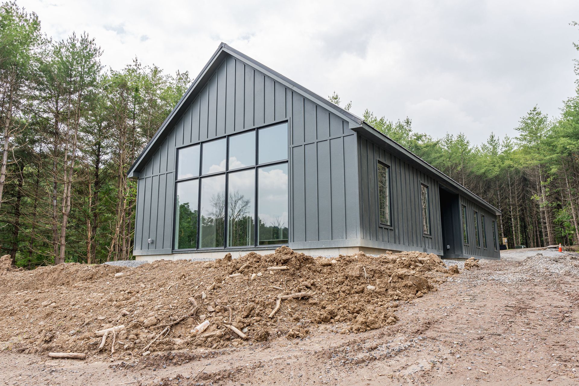 A large house is sitting on top of a dirt hill in the middle of a forest.