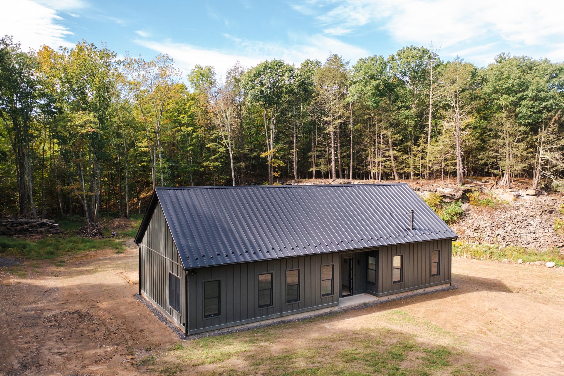 A large house is sitting in the middle of a field in the middle of a forest.