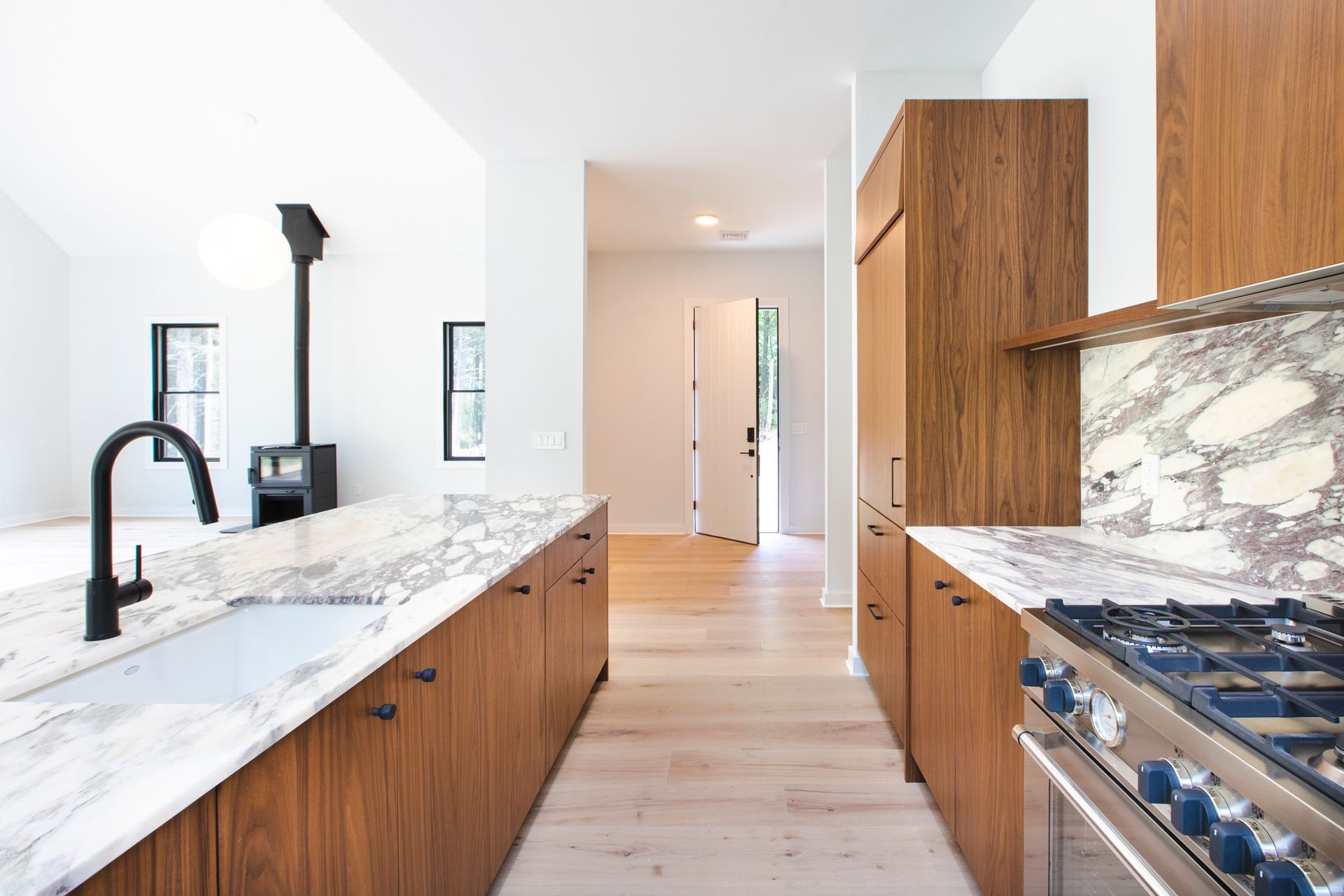 A kitchen with wooden cabinets , marble counter tops , a stove and a sink.