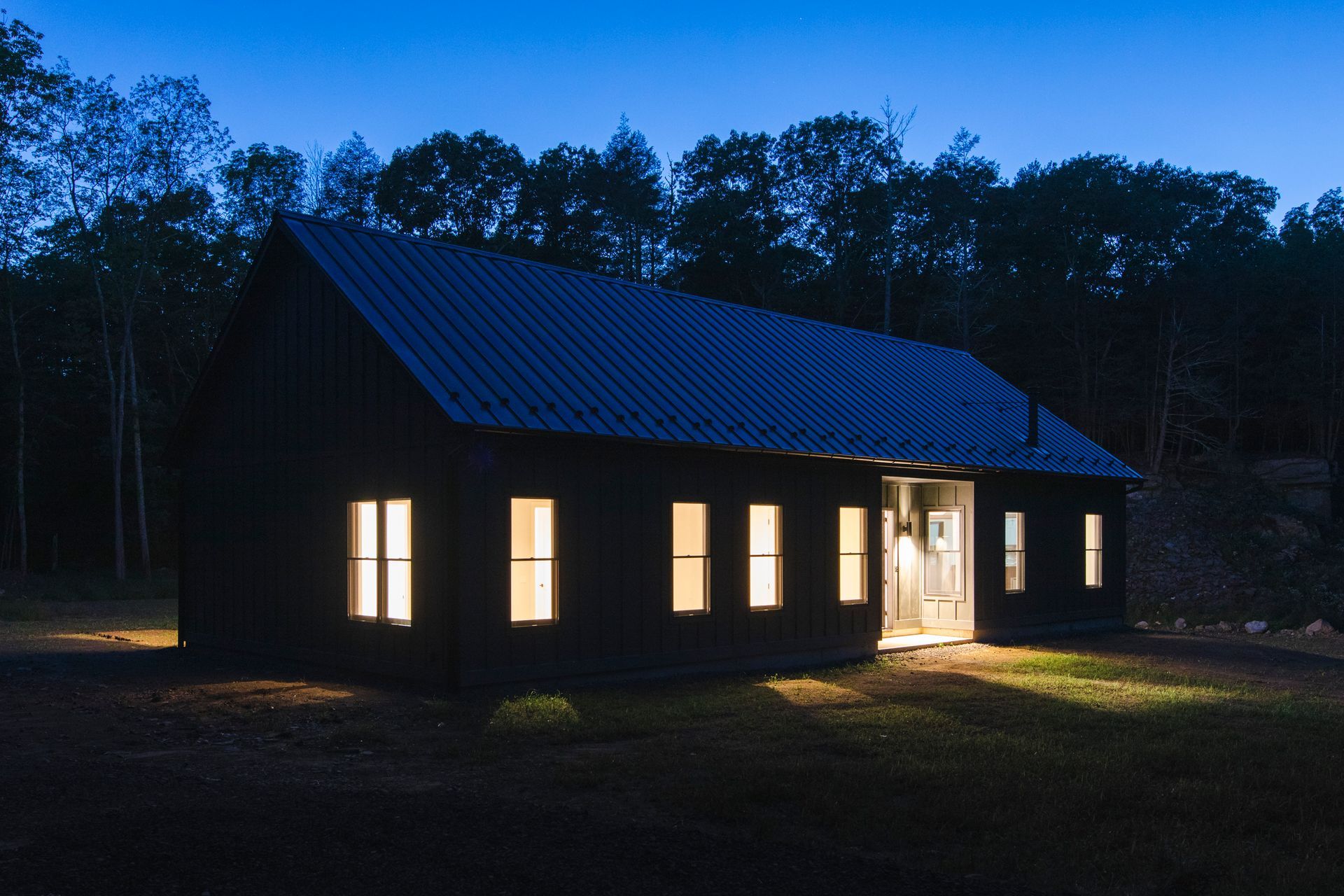 A black house is lit up at night with trees in the background