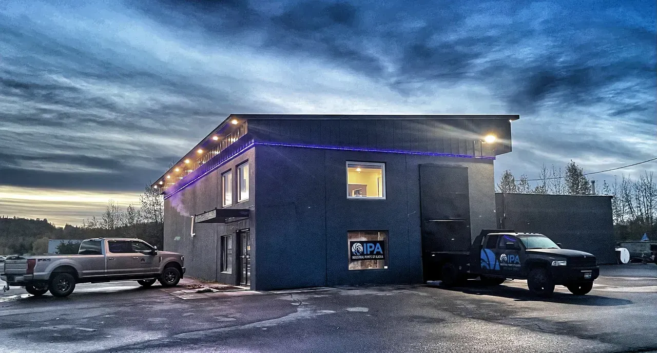 Two trucks are parked in front of a building at night.