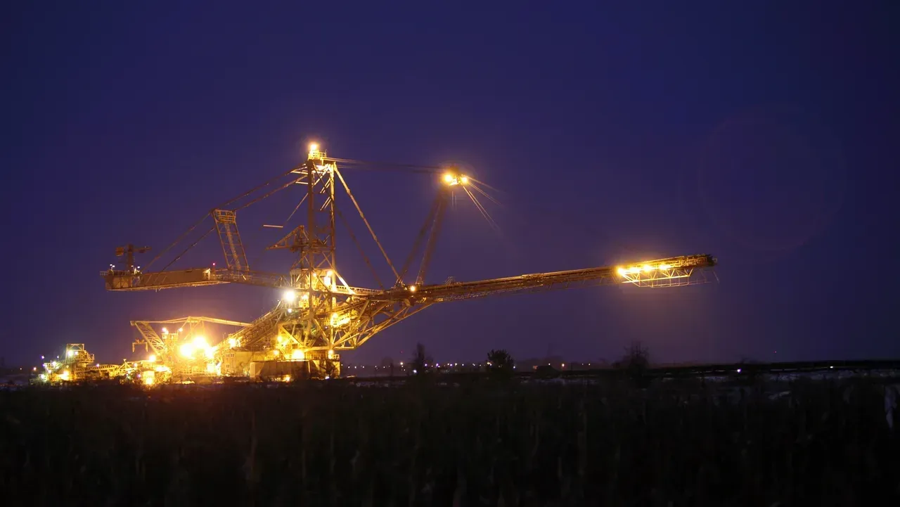 A large excavator is lit up at night in a field.