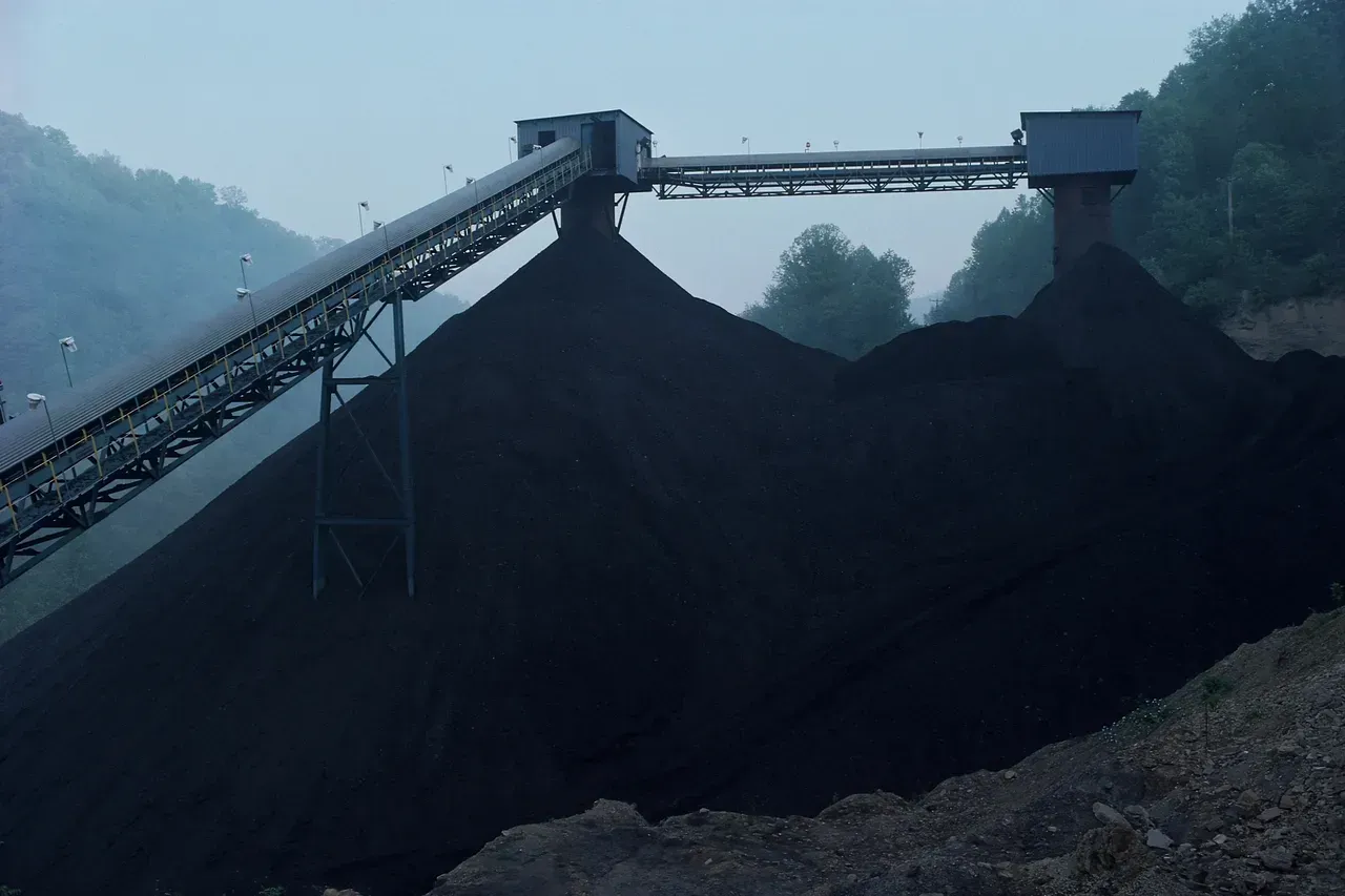 A large pile of coal is being loaded onto a conveyor belt at a coal mine.