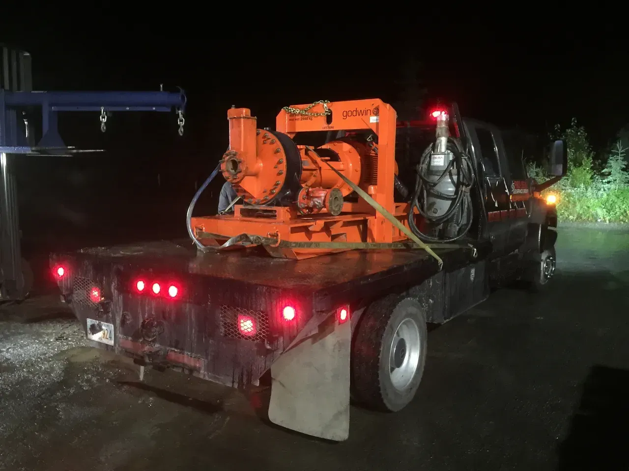 A tow truck is carrying a large orange machine on the back of it.