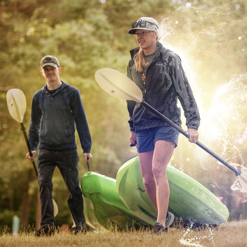 Two people with paddles stand near green kayaks outdoors.