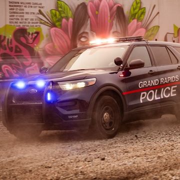 Grand Rapids Police SUV, blue lights flashing, driving on dirt road, graffiti background.