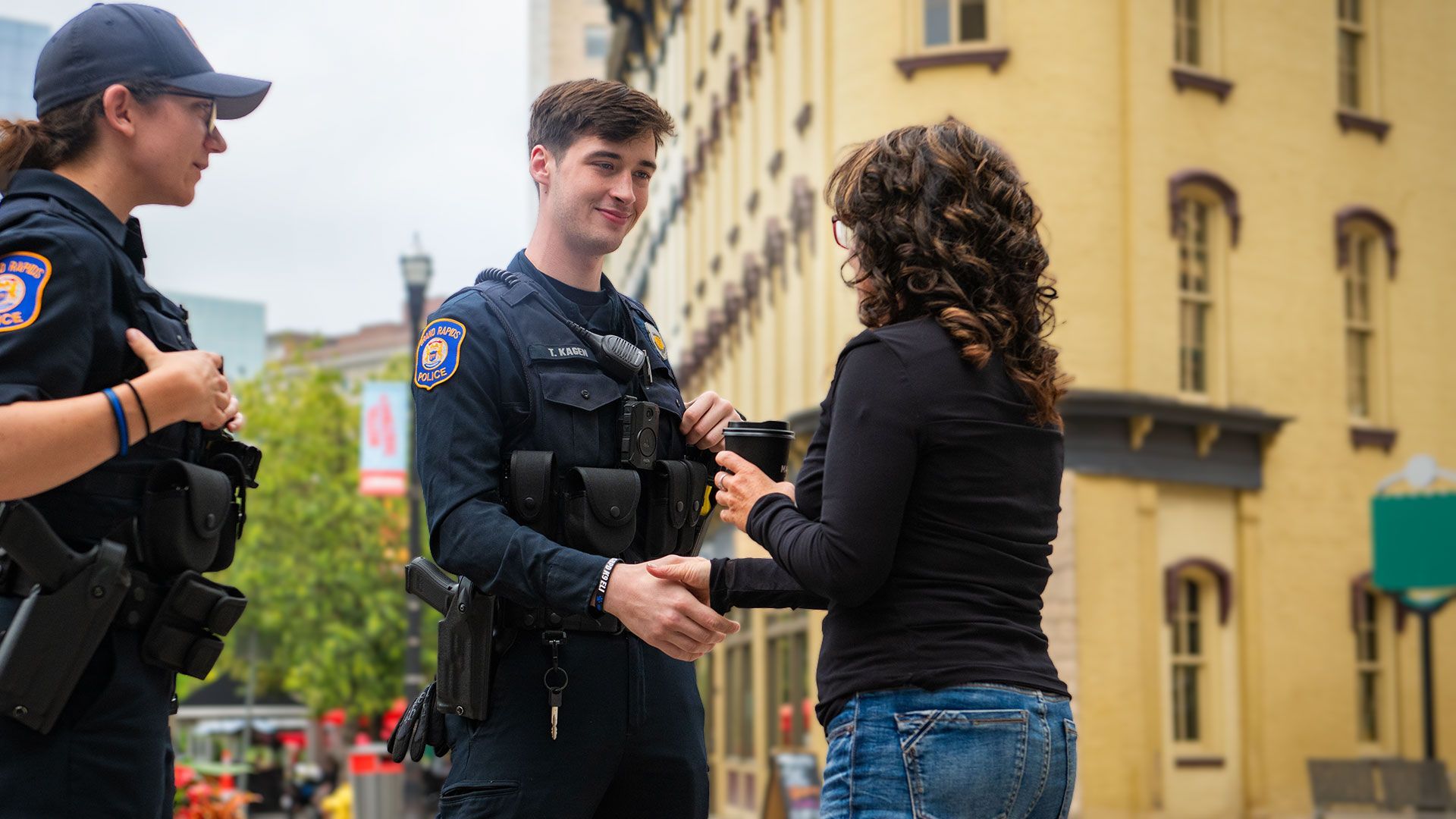 Two police officers talking to a civilian, shaking hands in a city.