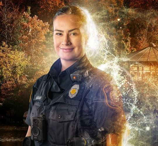 Police officer in uniform smiling outdoors, illuminated by glowing light.