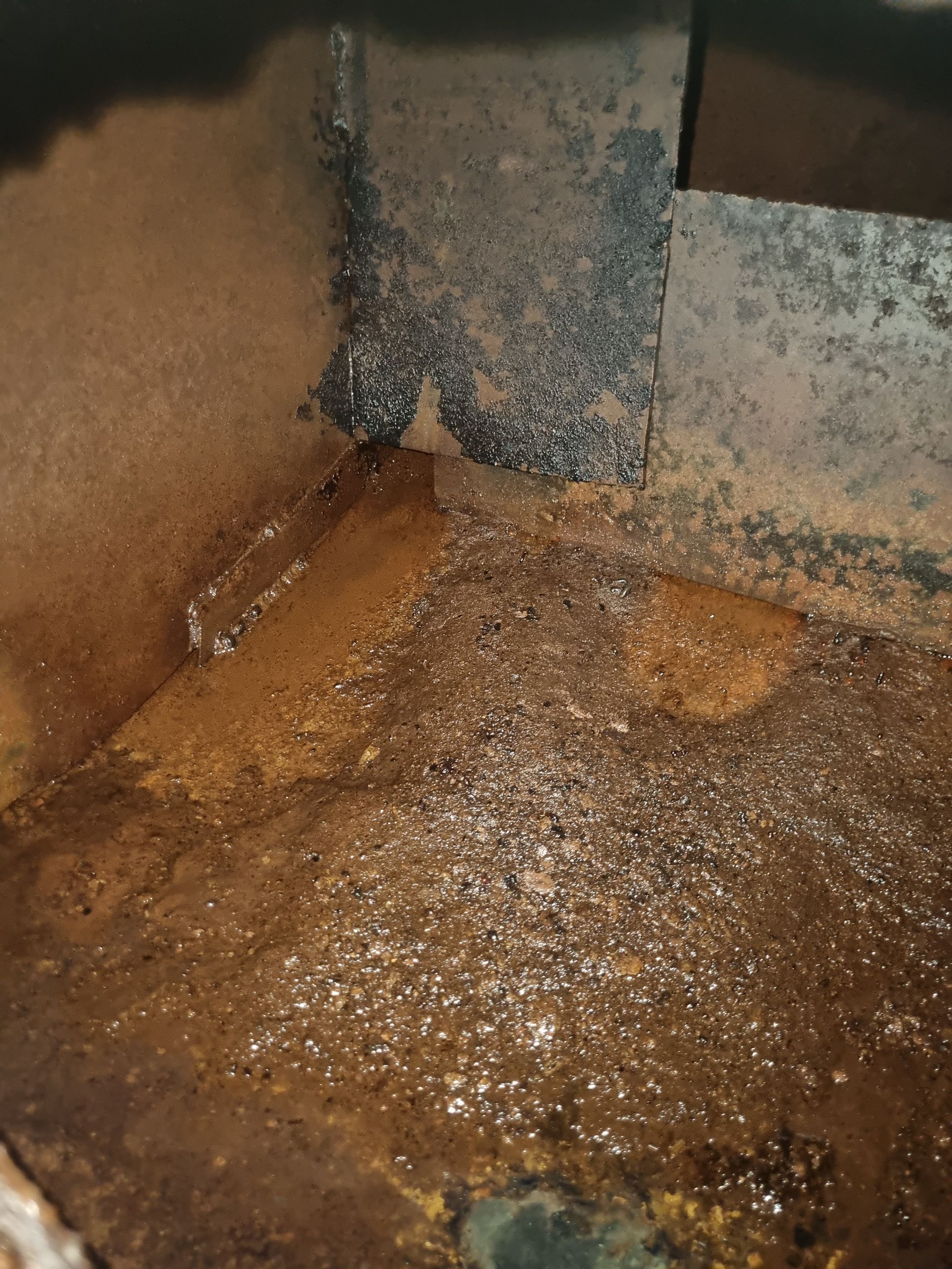 Rusty metal interior with liquid, possibly condensation, pooling at the bottom and corner.