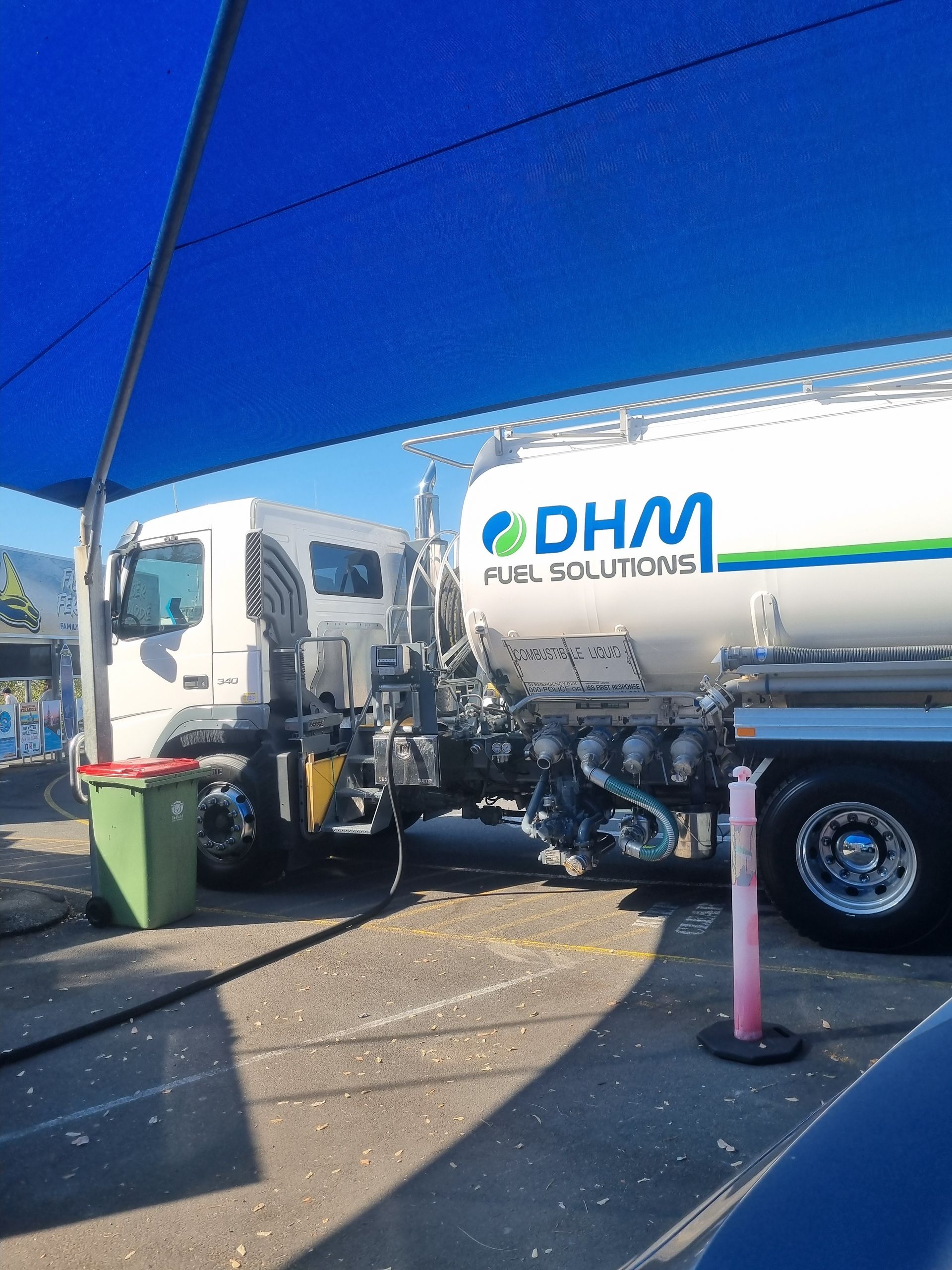 Fuel tanker truck parked under a blue shade, labeled