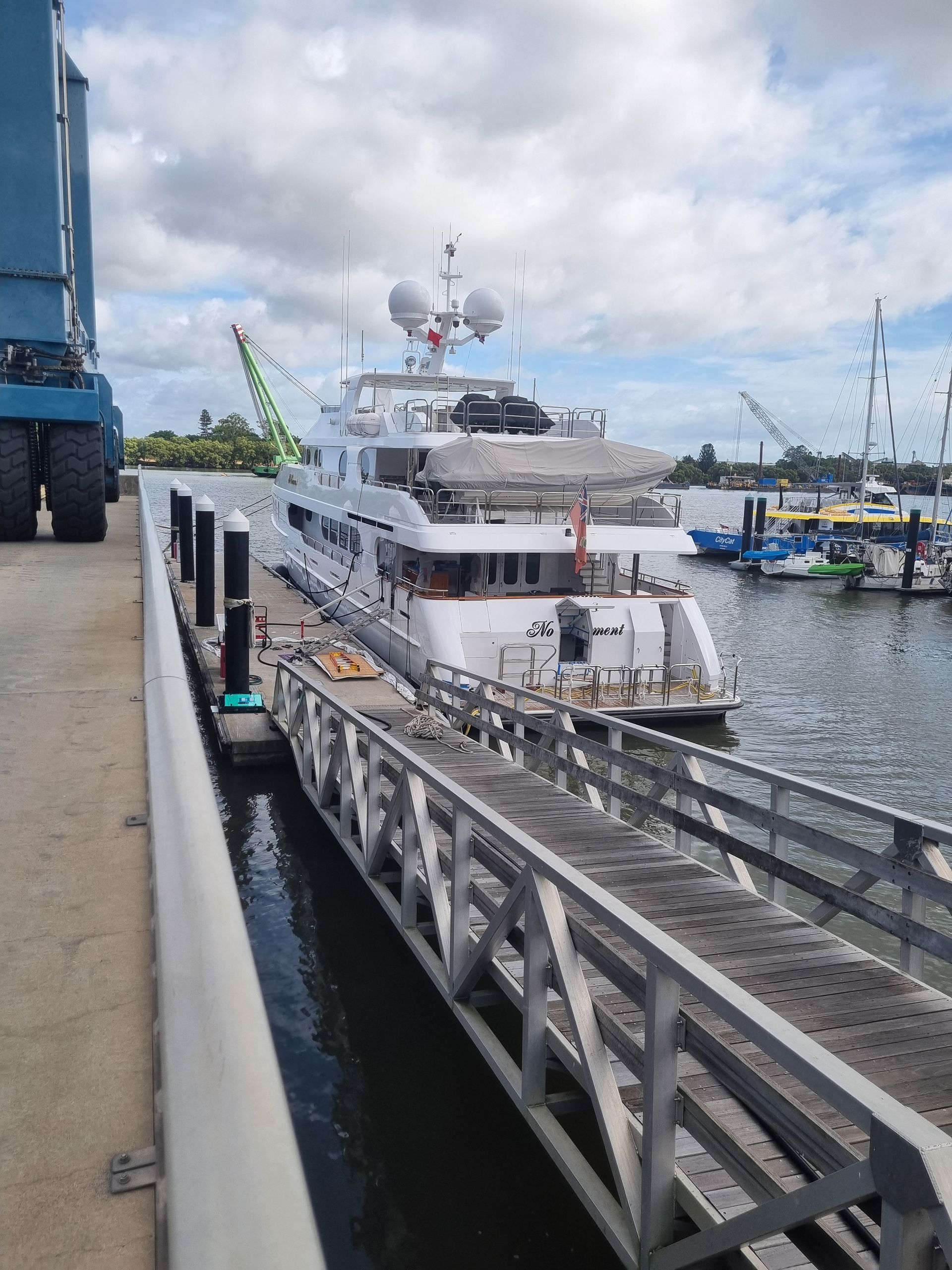 White yacht moored at a marina beside a metal dock under a cloudy sky