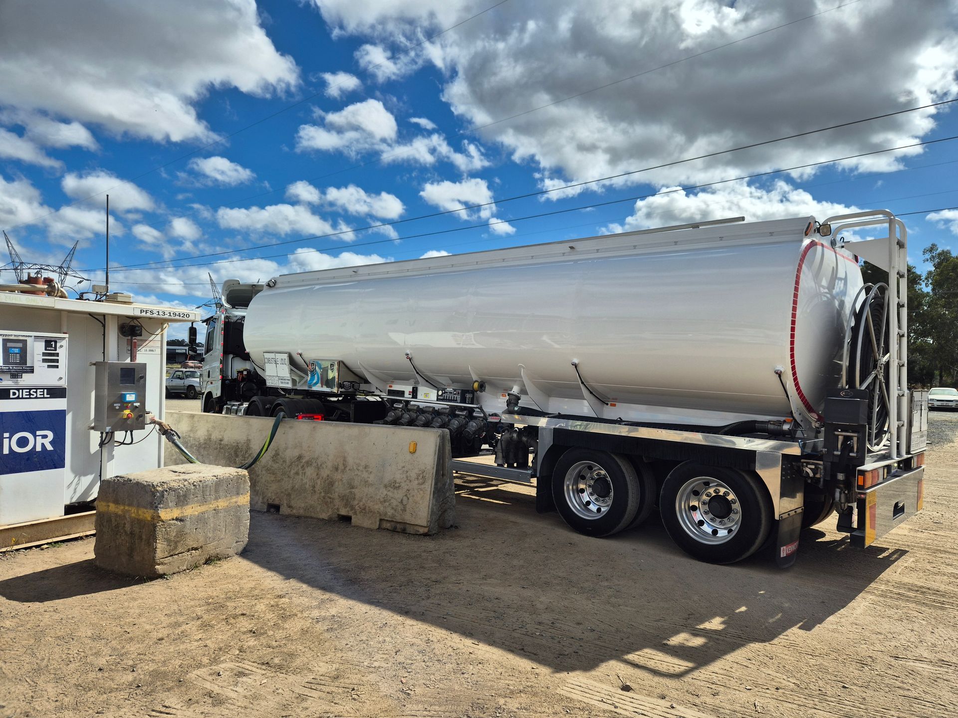 Silver tanker truck parked at a fuel station under a cloudy blue sky