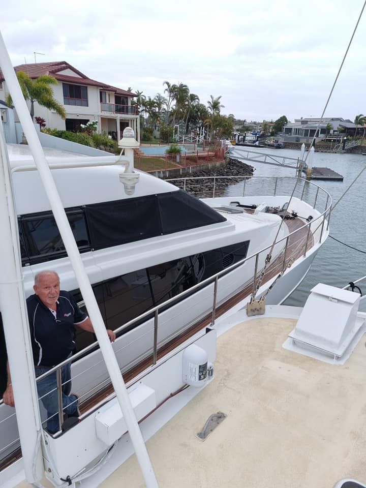 Man on a white yacht near a canal, with houses in the background. Cloudy day.