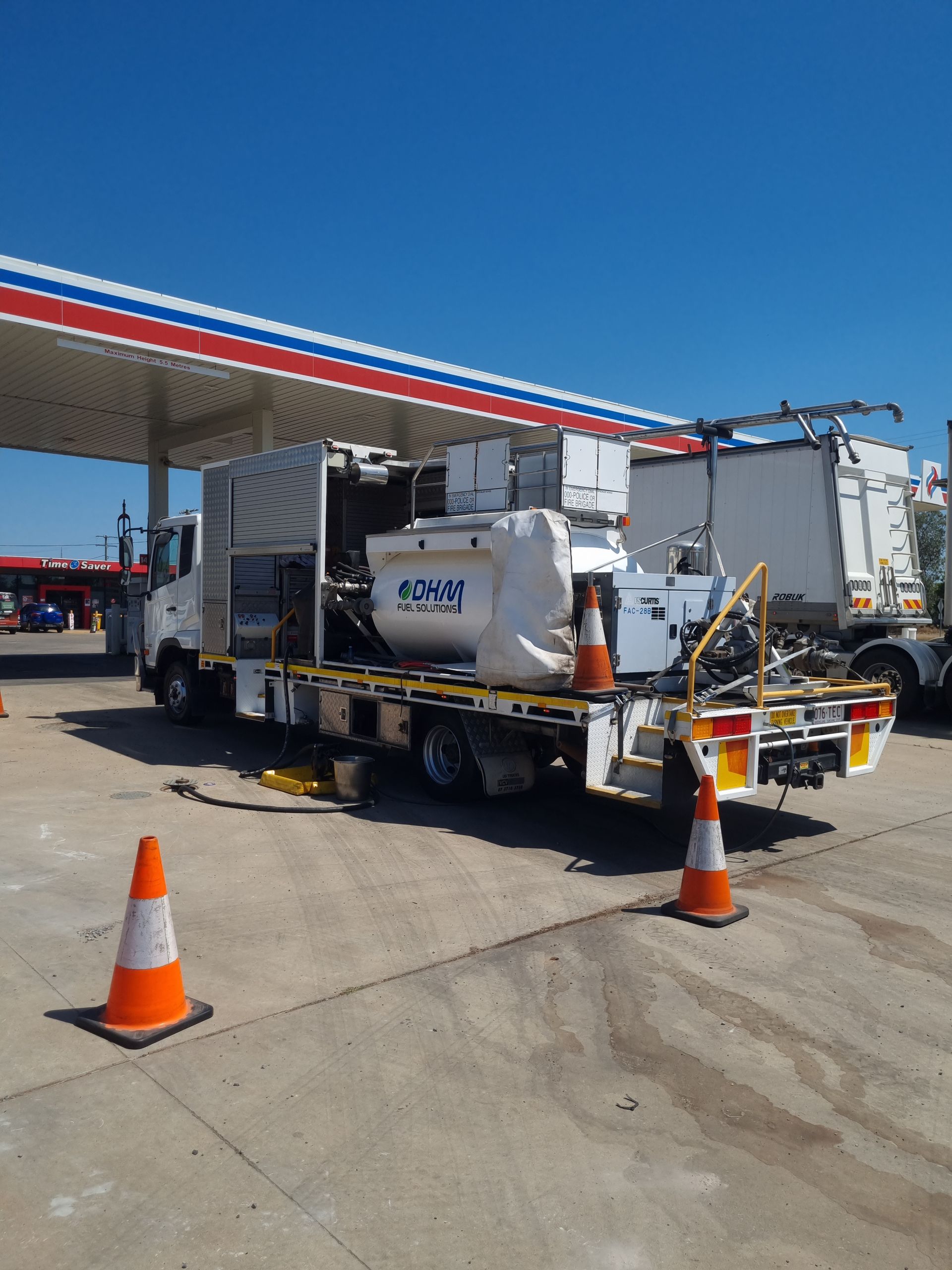 White truck with mounted equipment at a gas station. Orange cones placed near the vehicle.