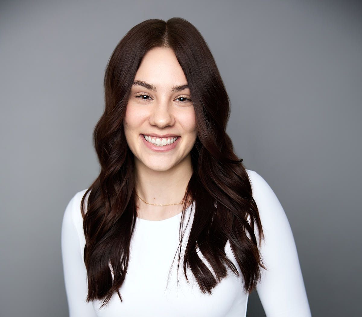 A woman with long brown hair is wearing a white shirt and black pants.